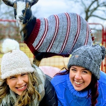 2 women with a goat in a sweater on top of them