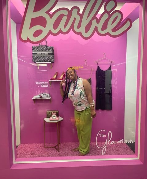 Black woman in green pants in a Barbie box photo booth.