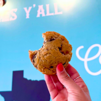 over saturated cookie being held by a hand with a teal Texan mural wall in the background.