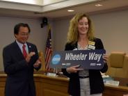 Kathryn Wheeler holding a street sign that says Wheeler Way