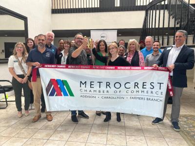 People holding Metrocrest Chamber of Commerce sign with giant scissors. 