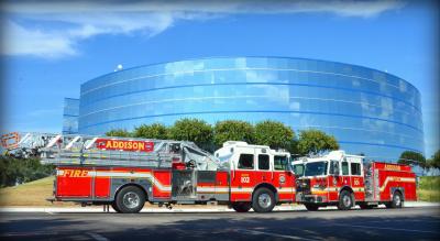 Two fire trucks parked in front of a large glass building on a sunny day