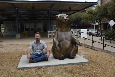 Man sitting next to bear statue