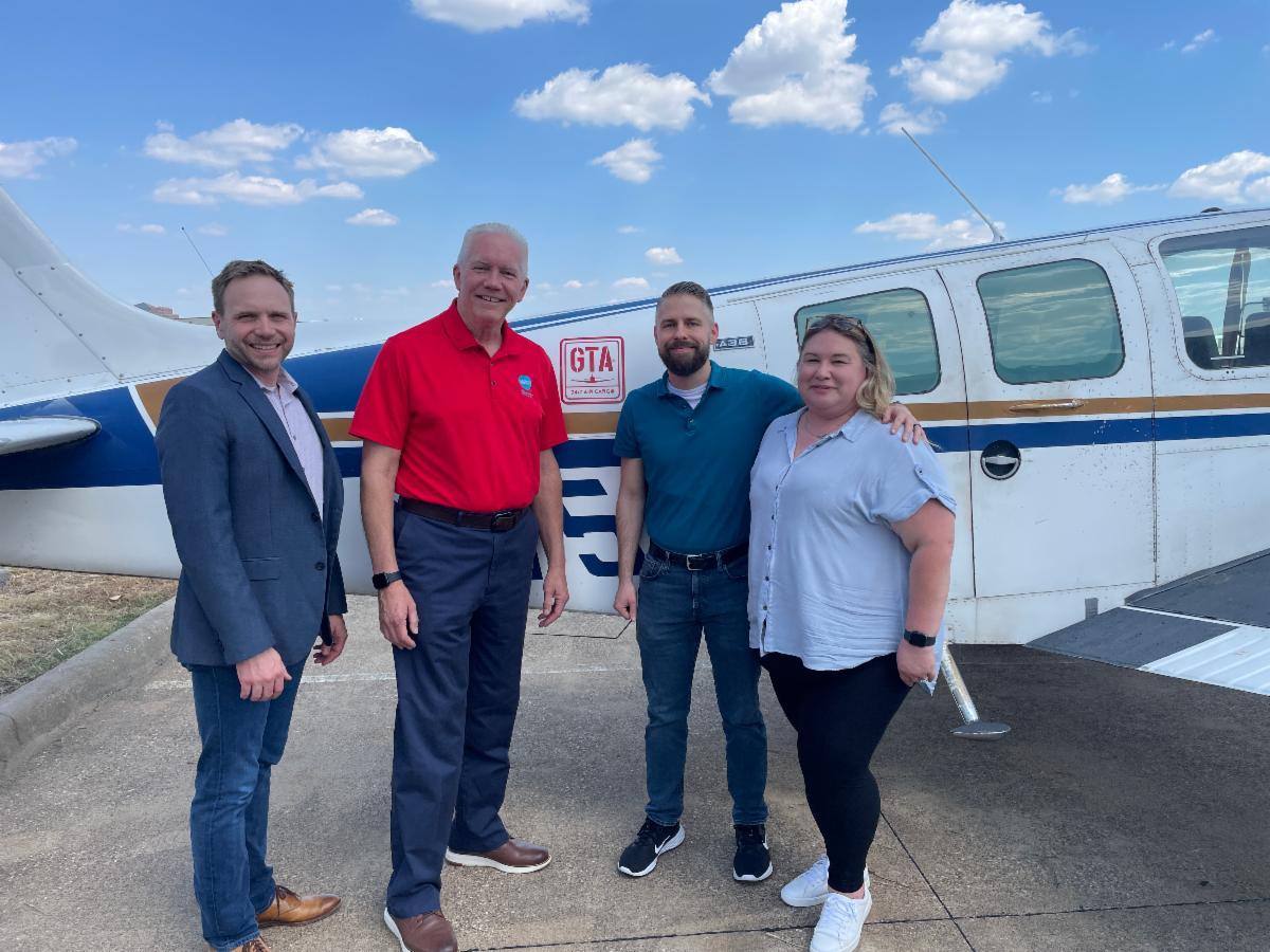 Three men and one woman standing in front of a small airplane