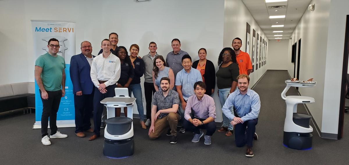 Group of people standing with Bear Robotics robots