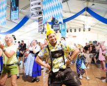 Man in leiderhosen and a chicken hat dancing in the big tent at Addison Oktoberfest