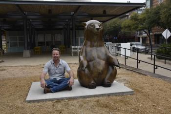 Man sitting next to bear statue