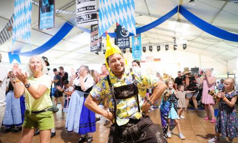 Man in leiderhosen and a chicken hat dancing in the big tent at Addison Oktoberfest